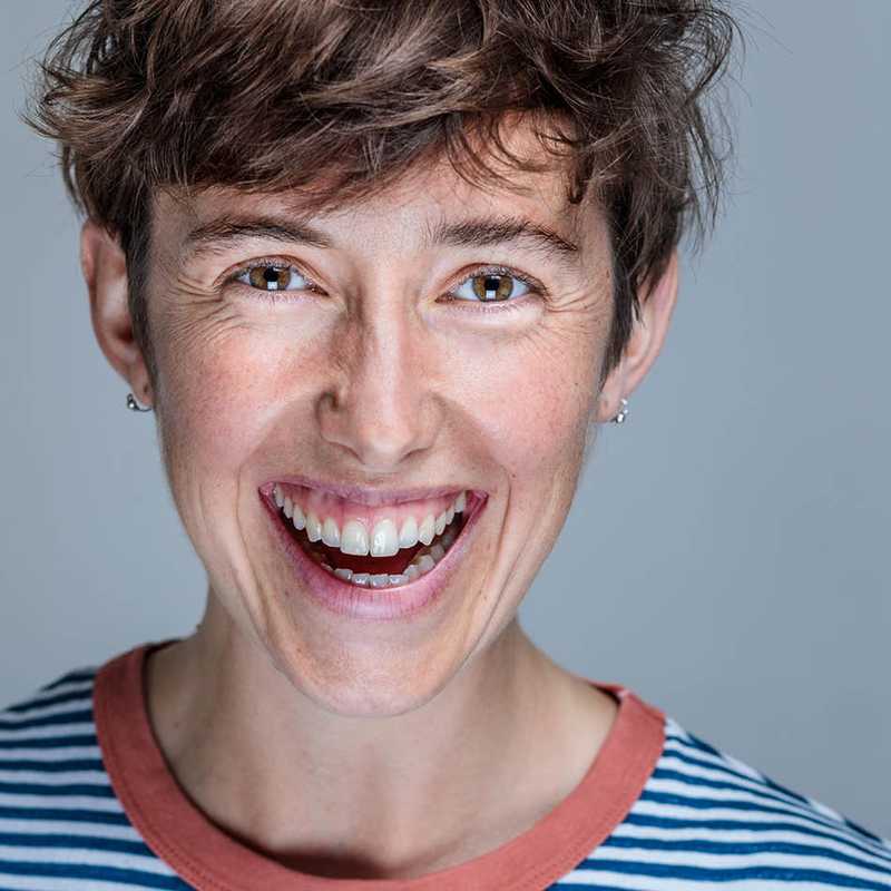An image of Claire Parry smiling gleefully in a blue and white striped top. White woman with short brown hair and brown eyes. 