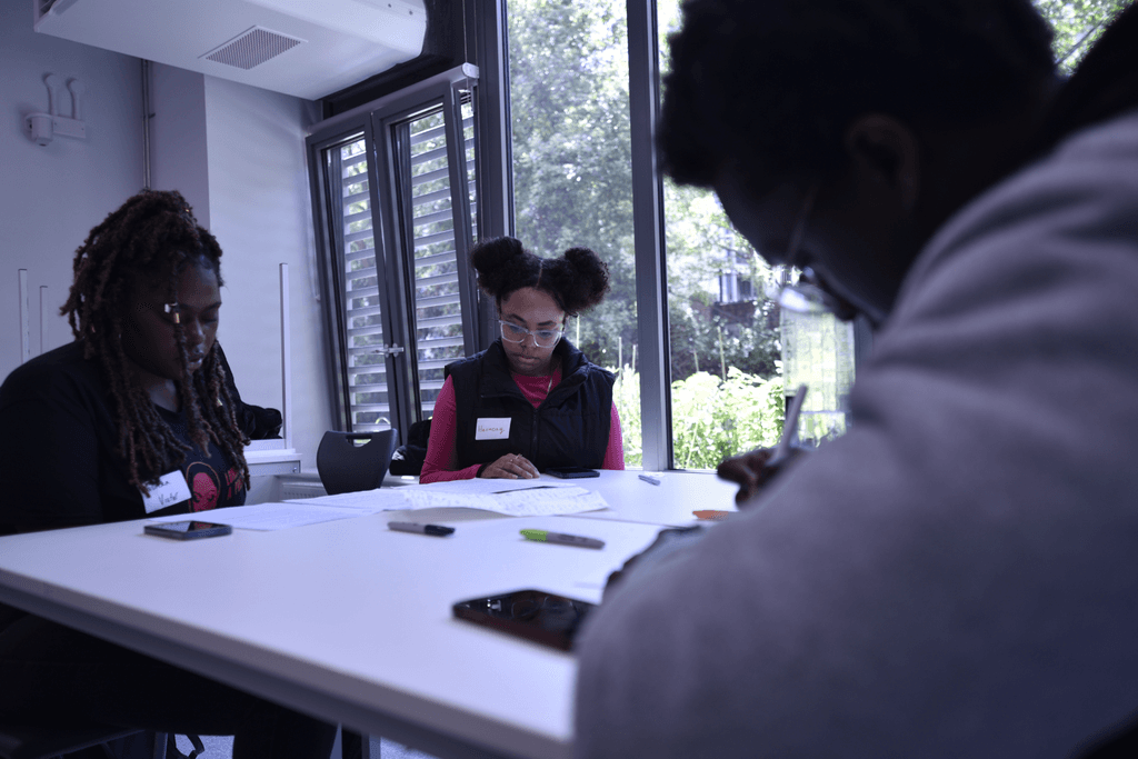 A young black person from Avenues Youth group working on their script during Start Your Script in a bright white painted room with windows.