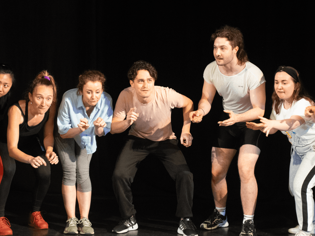 A group of masterclass members performing a short piece of devised work, all at different levels standing in a line.