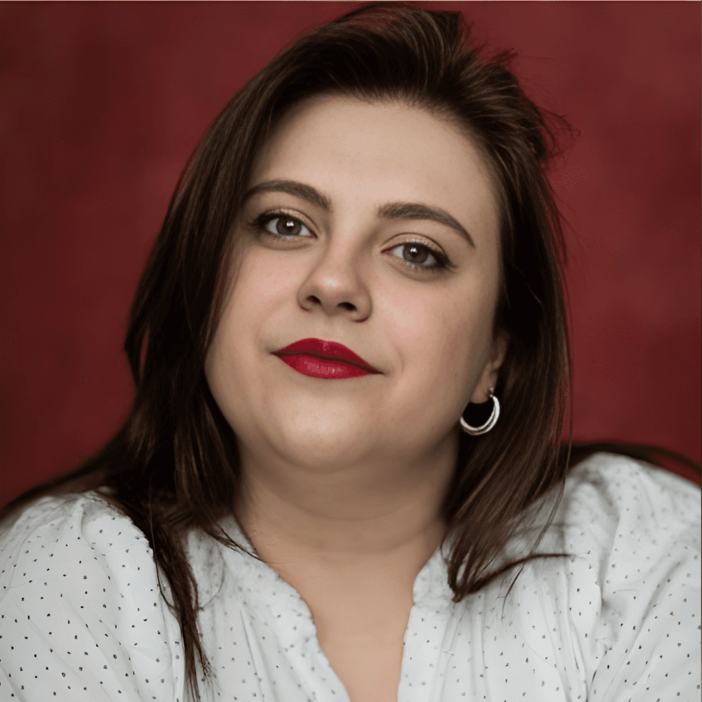 Headshot of Madison Parker. Madison has long dark hair and is wearing a white top with small black dots against a plain red background.