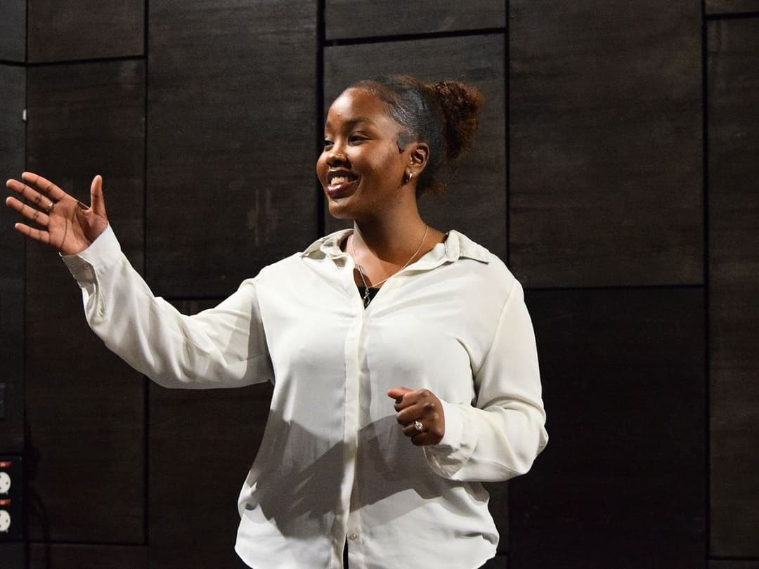Savannah, a woman in a white blouse, gestures while acting as part of Script Scratch