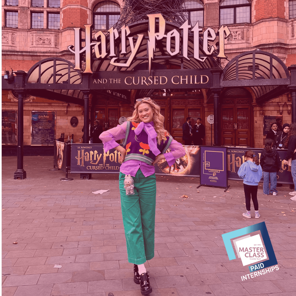 A young woman standing in front the Palace Theatre, dressed in purple and green