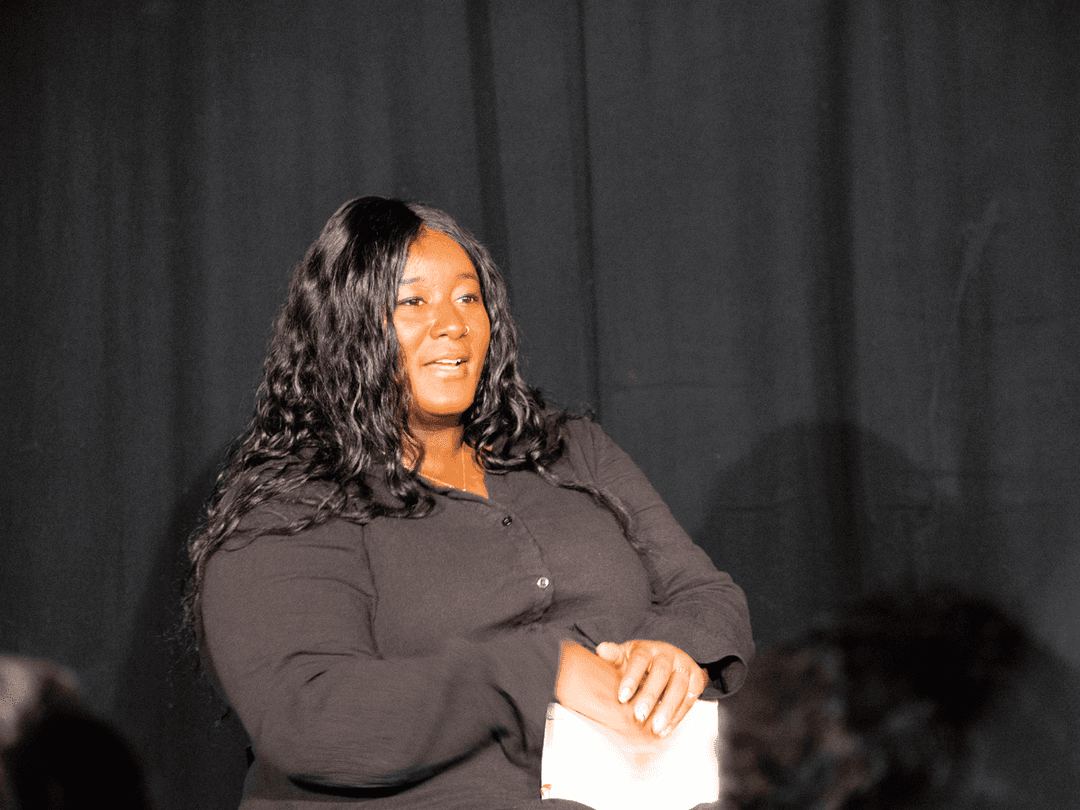 Yolanda Mercy sat on a chair with a notebook in her hands. A black woman with long black wavey hair, wearing a black buttoned dress.