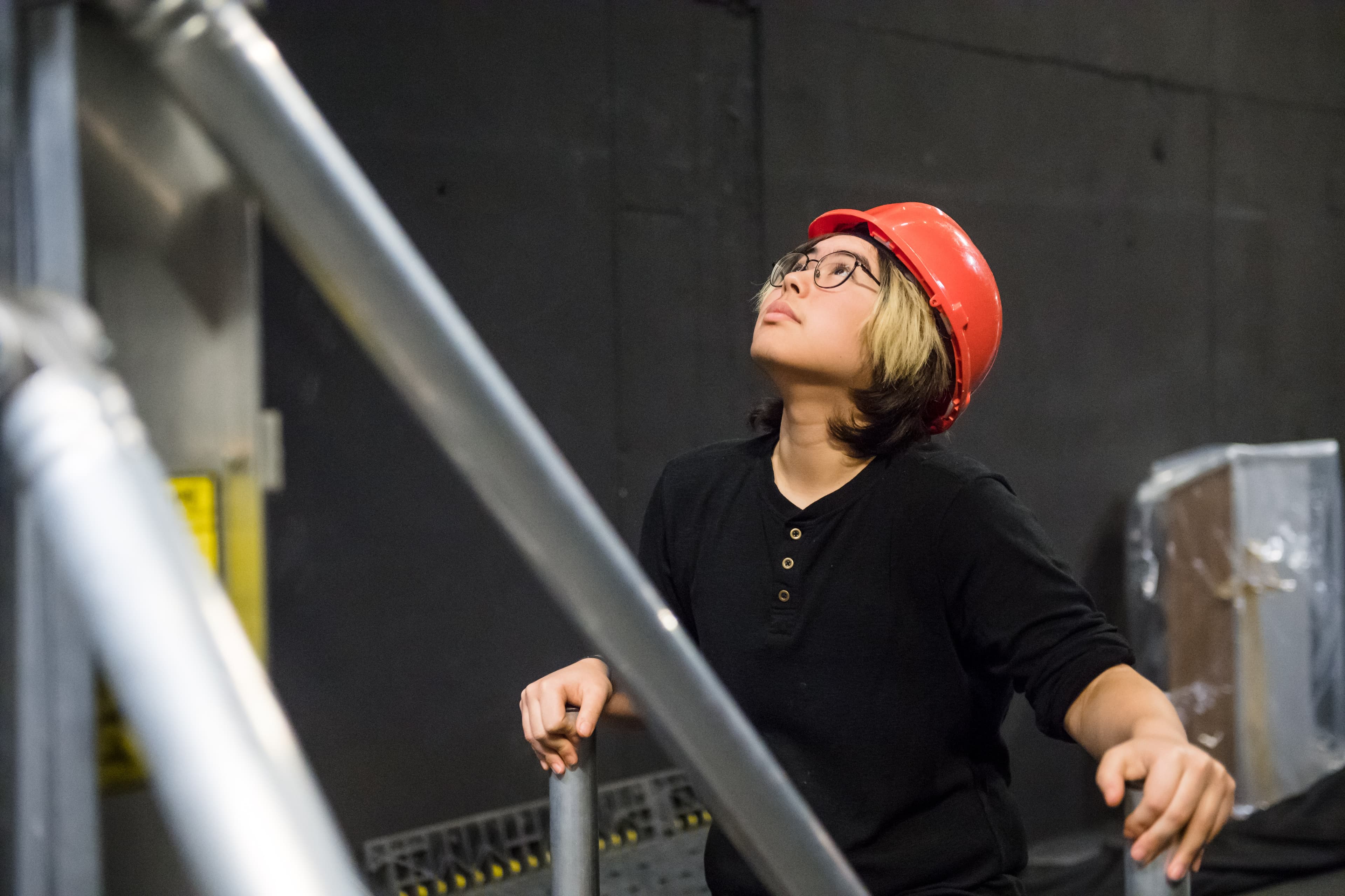 A young person in a hard hat working backstage in a theatre.