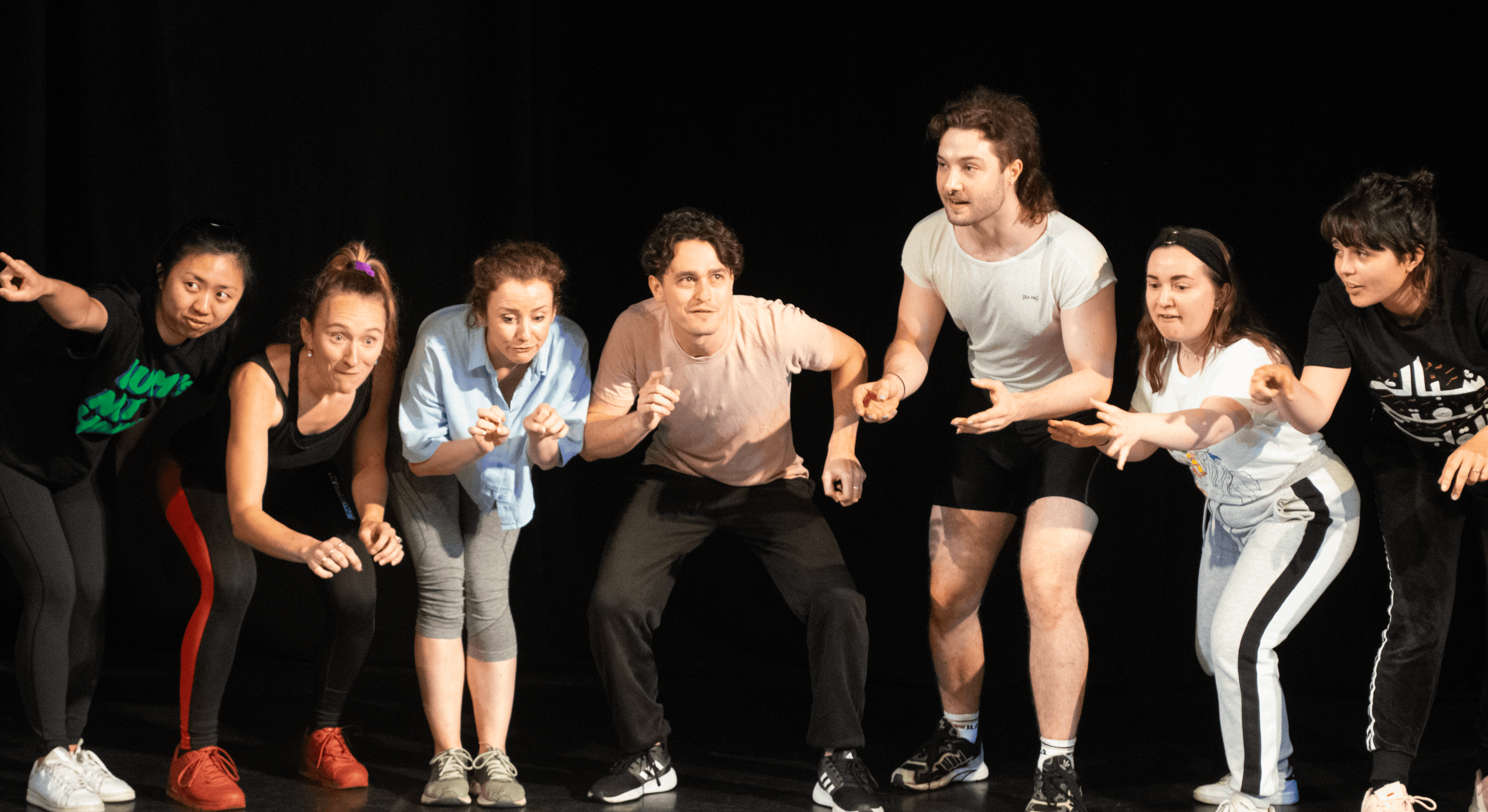 A group of masterclass members performing a short piece of devised work, all at different levels standing in a line.