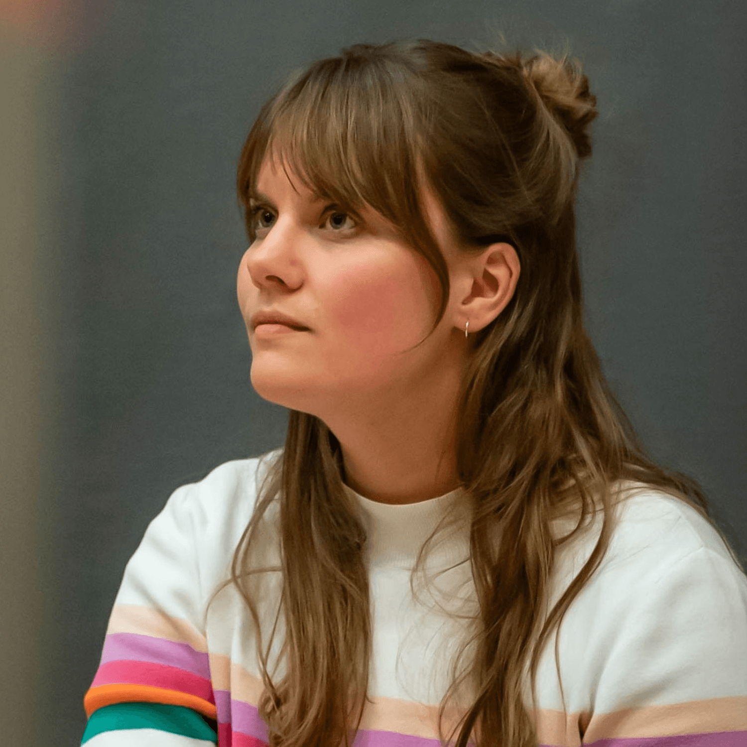 Frankie Brandshaw – a female with long hair and a colourful striped sweater – seated, engaged in a discussion against a green backdrop.