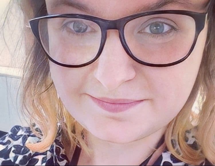 Holly Jevons close up headshot. Holly is a white woman with blonde and brown hair and black rimmed glasses.