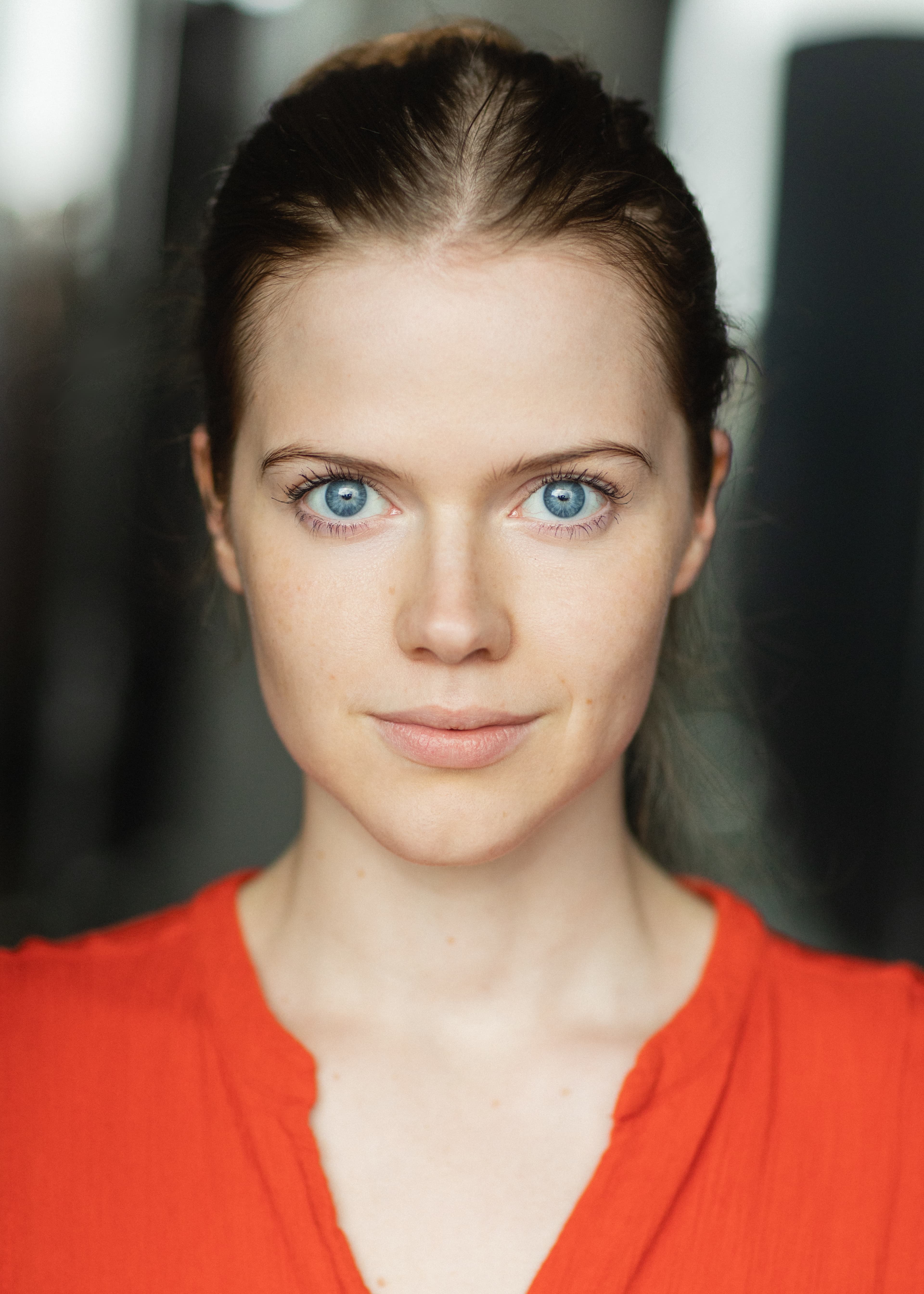 Katie Walker Cook Headshot. A white woman with blue eyes, tied back brown hair looking directly into the camera. She is wearing a bright orange top.