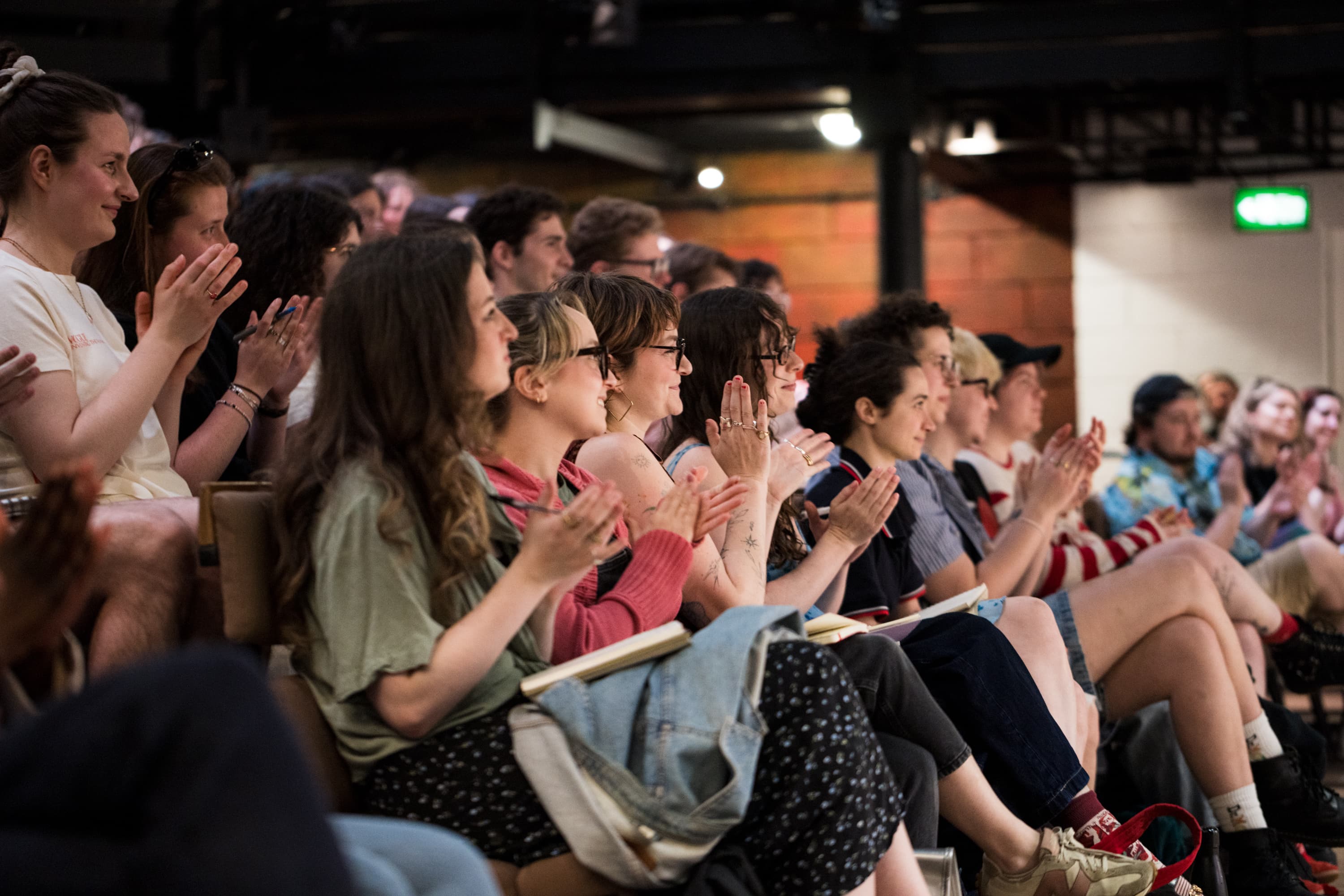 A group of young people clapping and smiling in a theatre setting.