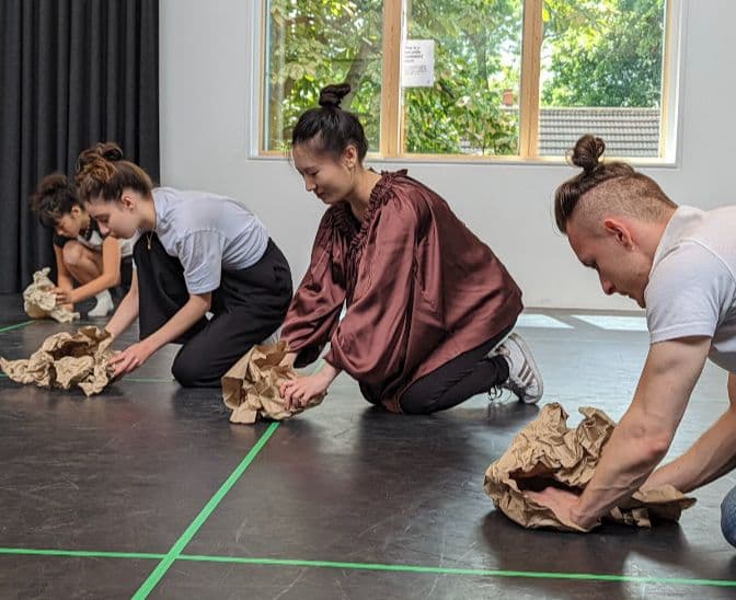 An image of people working with brown paper puppets.  A male and female smiling down at their puppets.