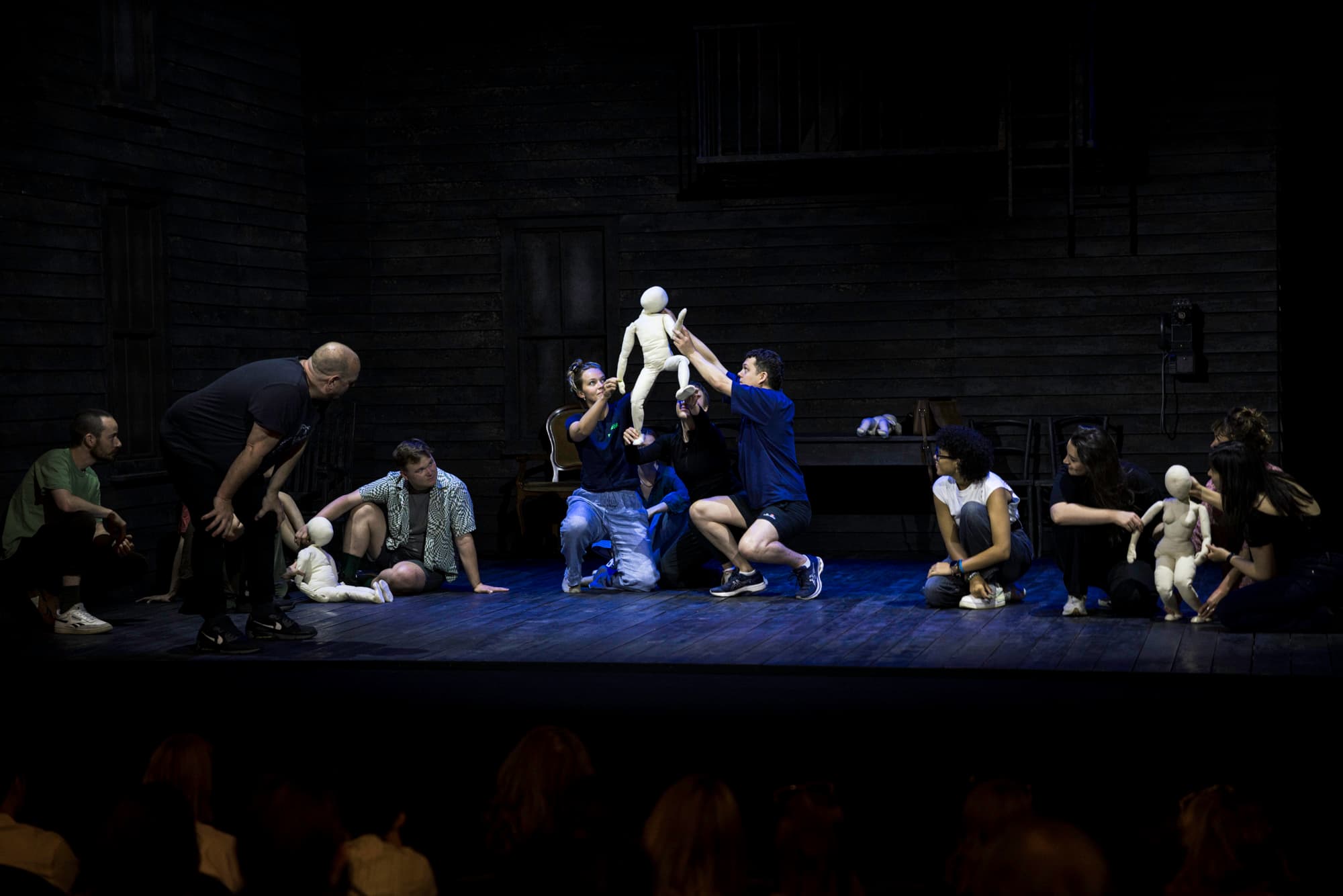 A group of young people working on a stage. Two people are holding a puppet in the air, as though it is jumping.