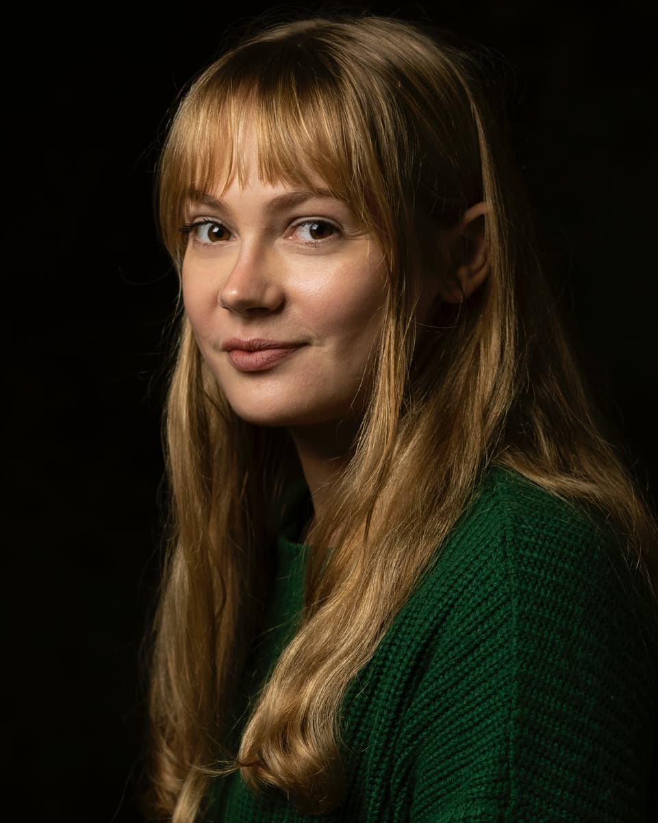 Shona Graham headshot, a white woman with long blonde hair and dark eyes, a closed smile. Wearing a dark green jumper.