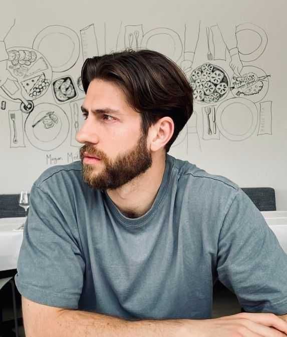 A white man with dark brown hair and a styled beard. Looking away from the camera.