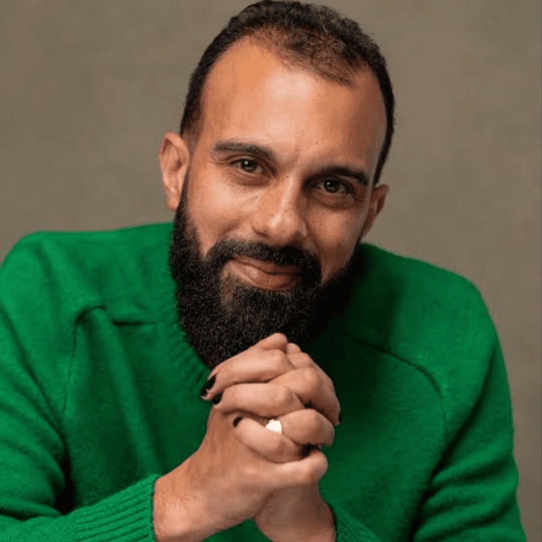 Headshot of Matthew Xia, a smiling bearded man wearing a green sweater, hands clasped, with black nail polish and a ring on his finger.