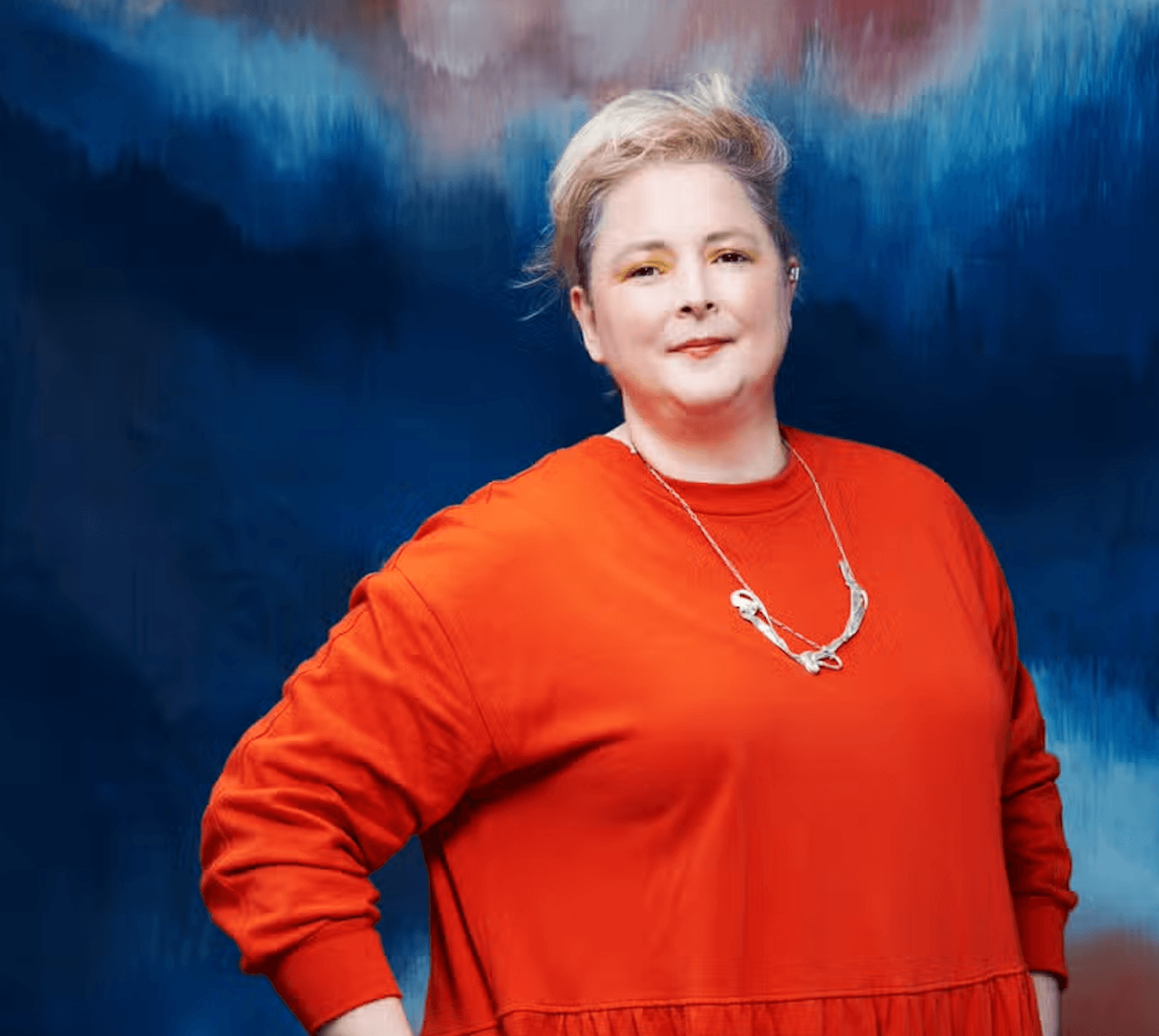 Siobhan McSweeney wearing a orange jumper against a blue/purple background
