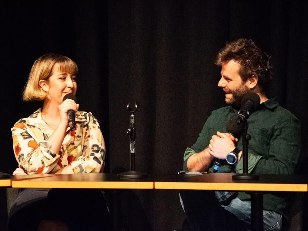 Claudia and Barra sit at a table with microphones during a discussion as part of Script Scratch