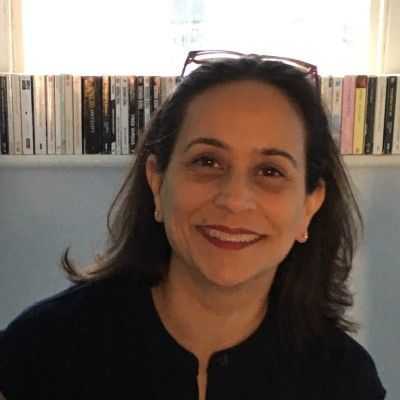 Photo of Clare Annamalai. Brown haired woman, wearing red lipstick with glasses on top of her head.